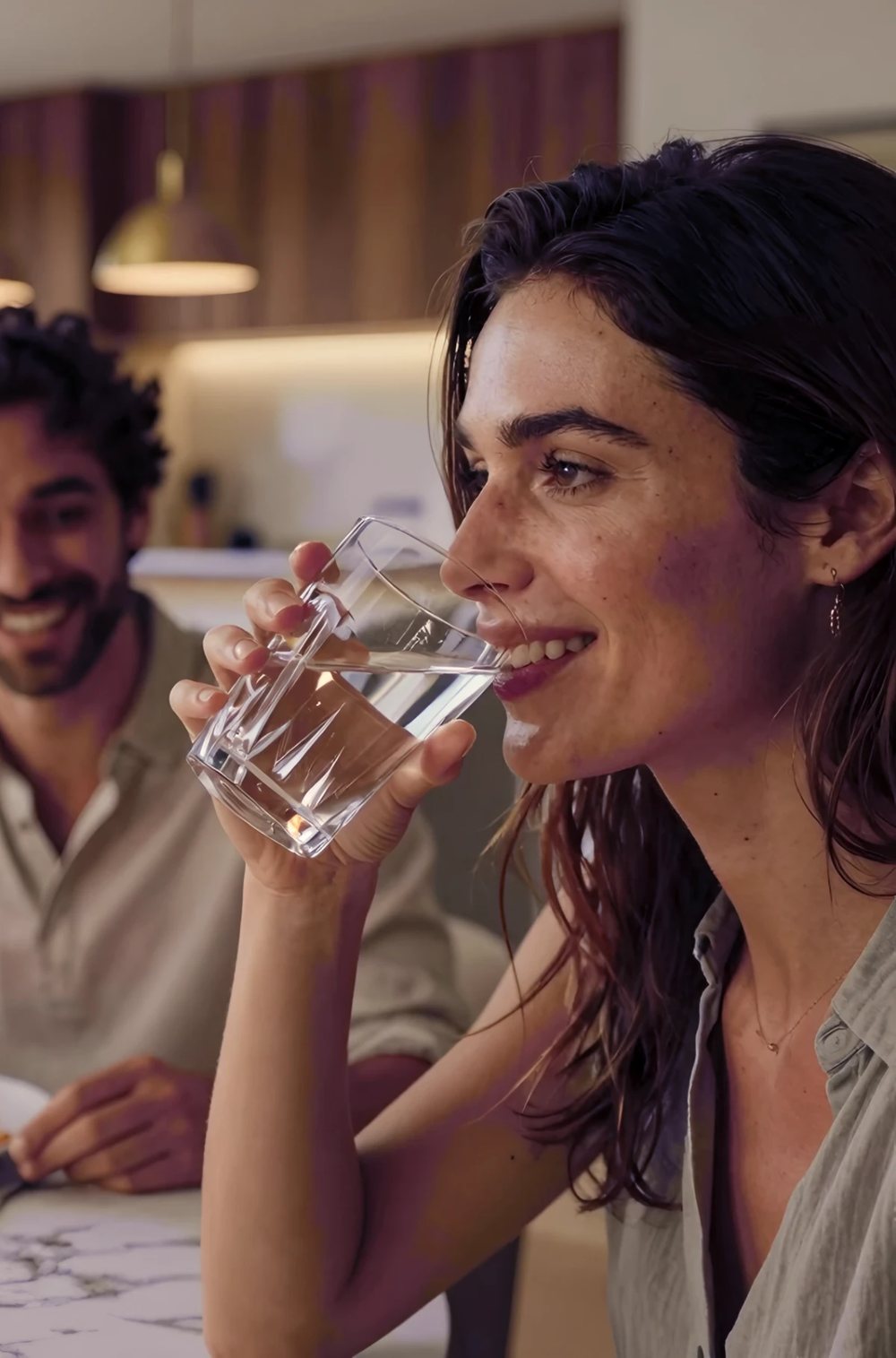 Servizio acqua a domicilio: una coppia a cena, lei beve acqua da un bicchiere di vetro